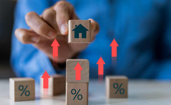 person holding wooden block with house icon and percentage symbols with red arrows indicating growth and increase related to real estate trends and property values 3 key factors