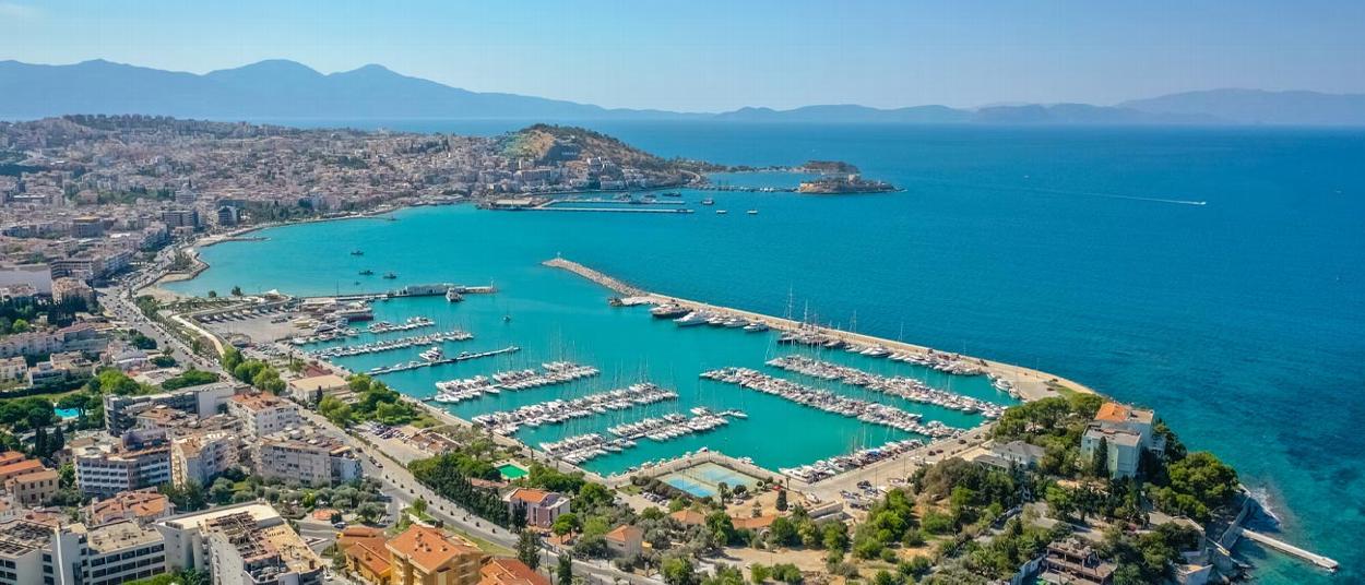 aerial view of a marina with numerous yachts docked in turquoise waters surrounded by coastal buildings and mountains in the background showcasing beautiful seaside location