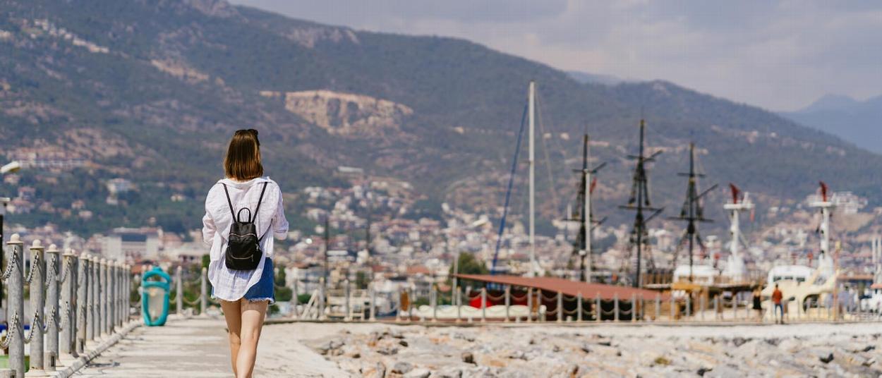 a woman walking along a seaside promenade with boats in the background enjoying the sunny weather and scenic views near five popular destinations