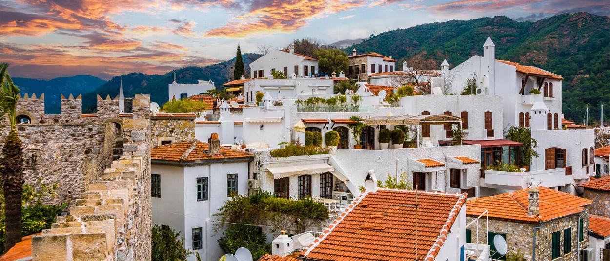 picturesque village with white buildings and red rooftops surrounded by mountains and sunset sky. tranquility and beauty captured in two different perspectives.