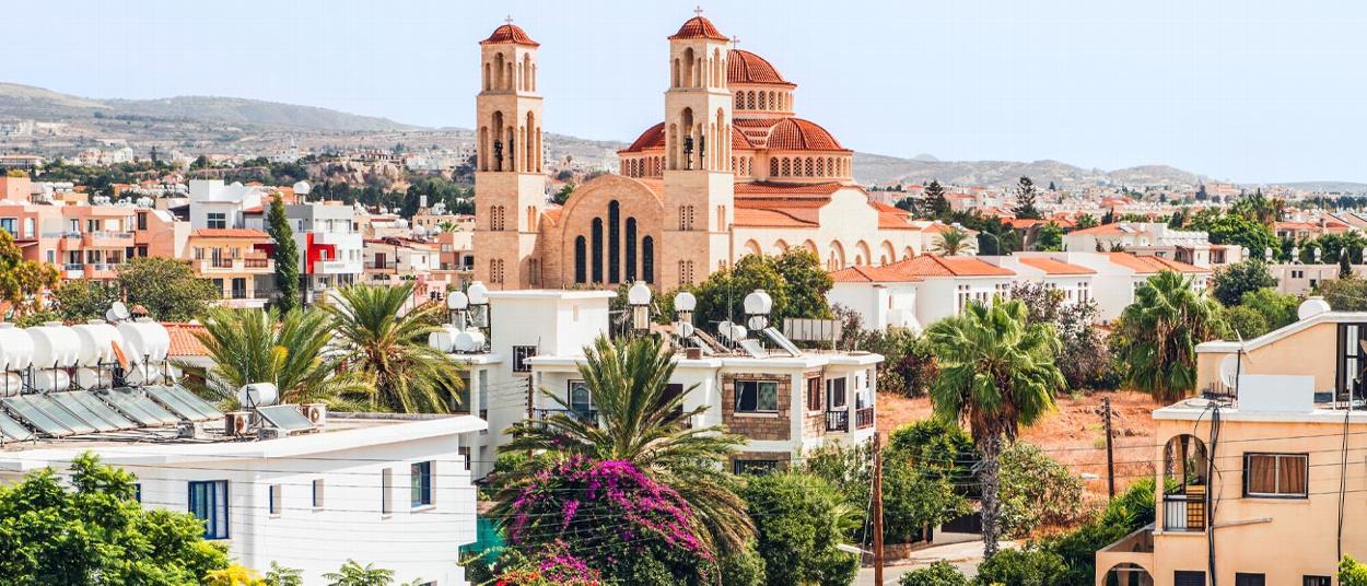 view of a city with white buildings palm trees and a large church with twin towers the scene captures sunny weather and urban landscape featuring architecture related to seven wonders of the world